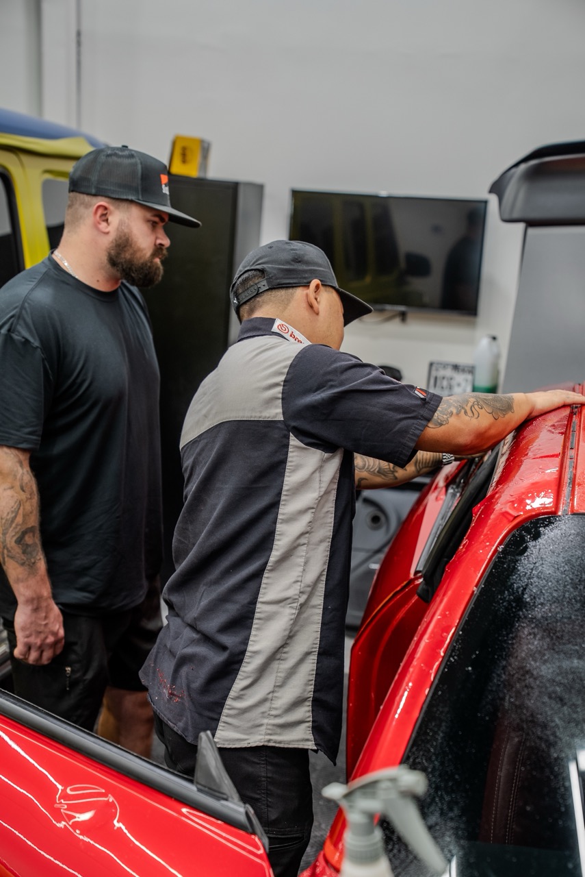 A paint protection film instructor guiding a student on applying PPF onto a vehicle